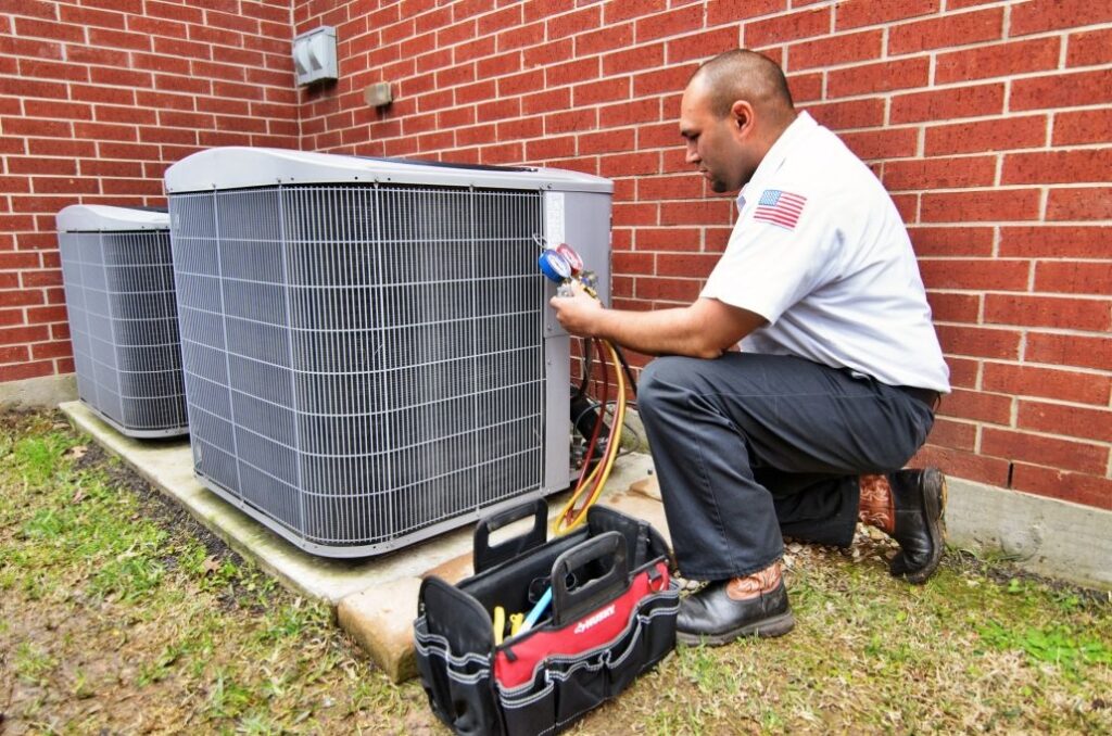 Male HVAC technician using tool to check an AC unit, outside on the side of a house.