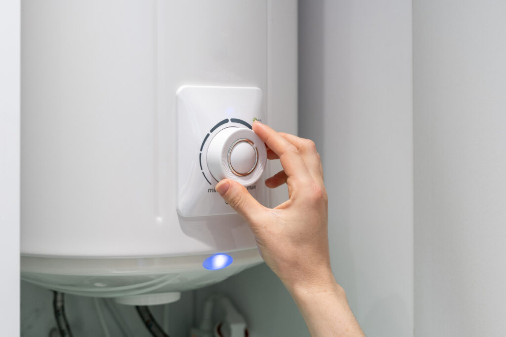 Cropped photo of female adjusting temperature on boiler hanging on wall, using control knob.